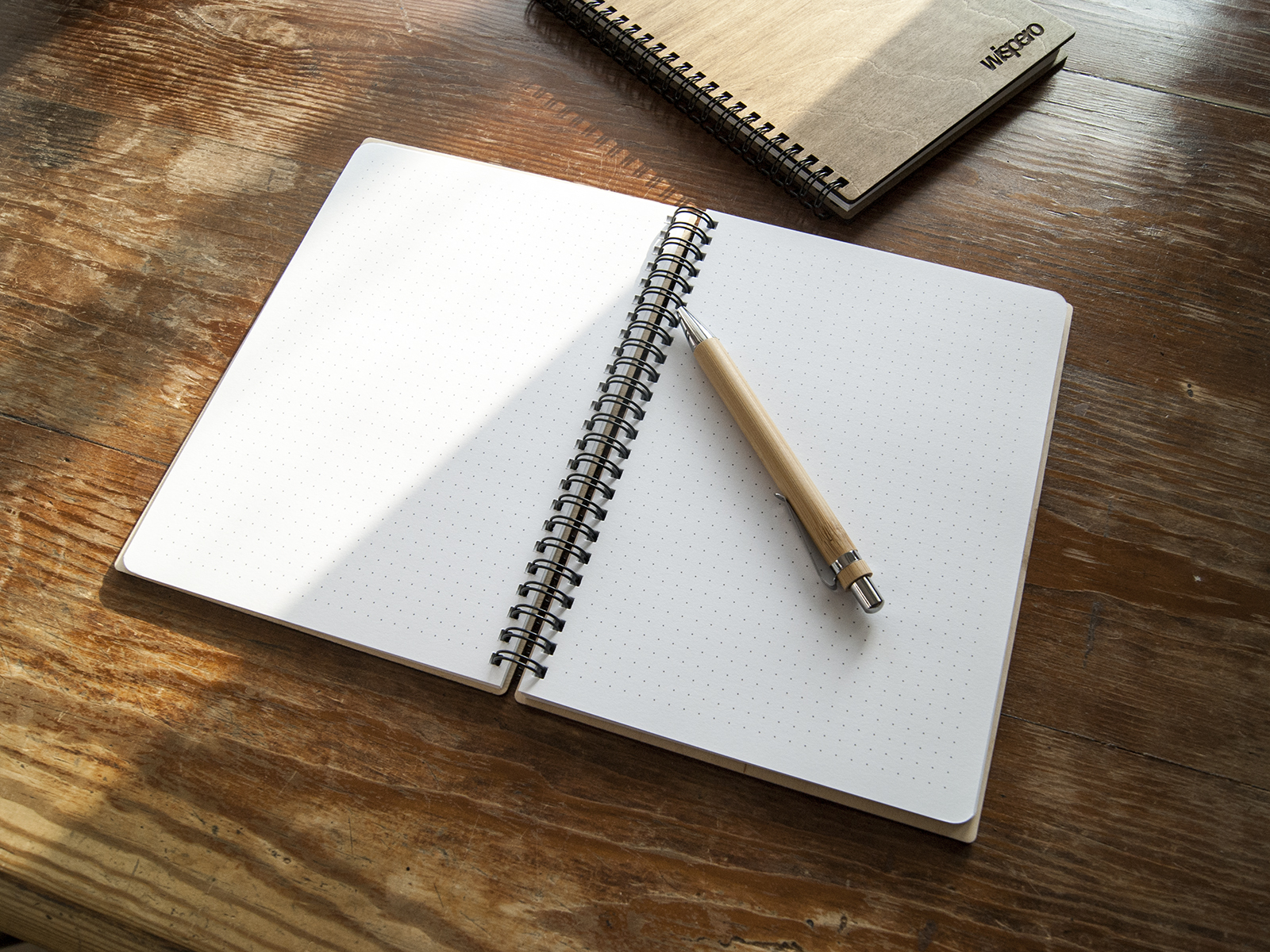 Otwarty notes A5 z kartkami w delikatną kropkę (dot grid) i drewnianym długopisem leżącym na stronie, w tle drugi zamknięty notes w drewnianej oprawie.